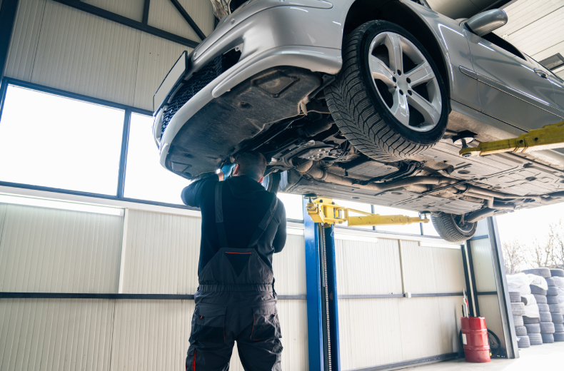 Serviceman checks car suspension on a column lift in car auto shop near Easton, PA.